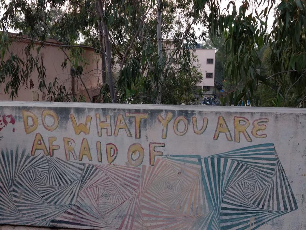 A piece of street art on a wall with the words "Do What You Are Afraid Of" above a series of interesting geometric shapes and handprints